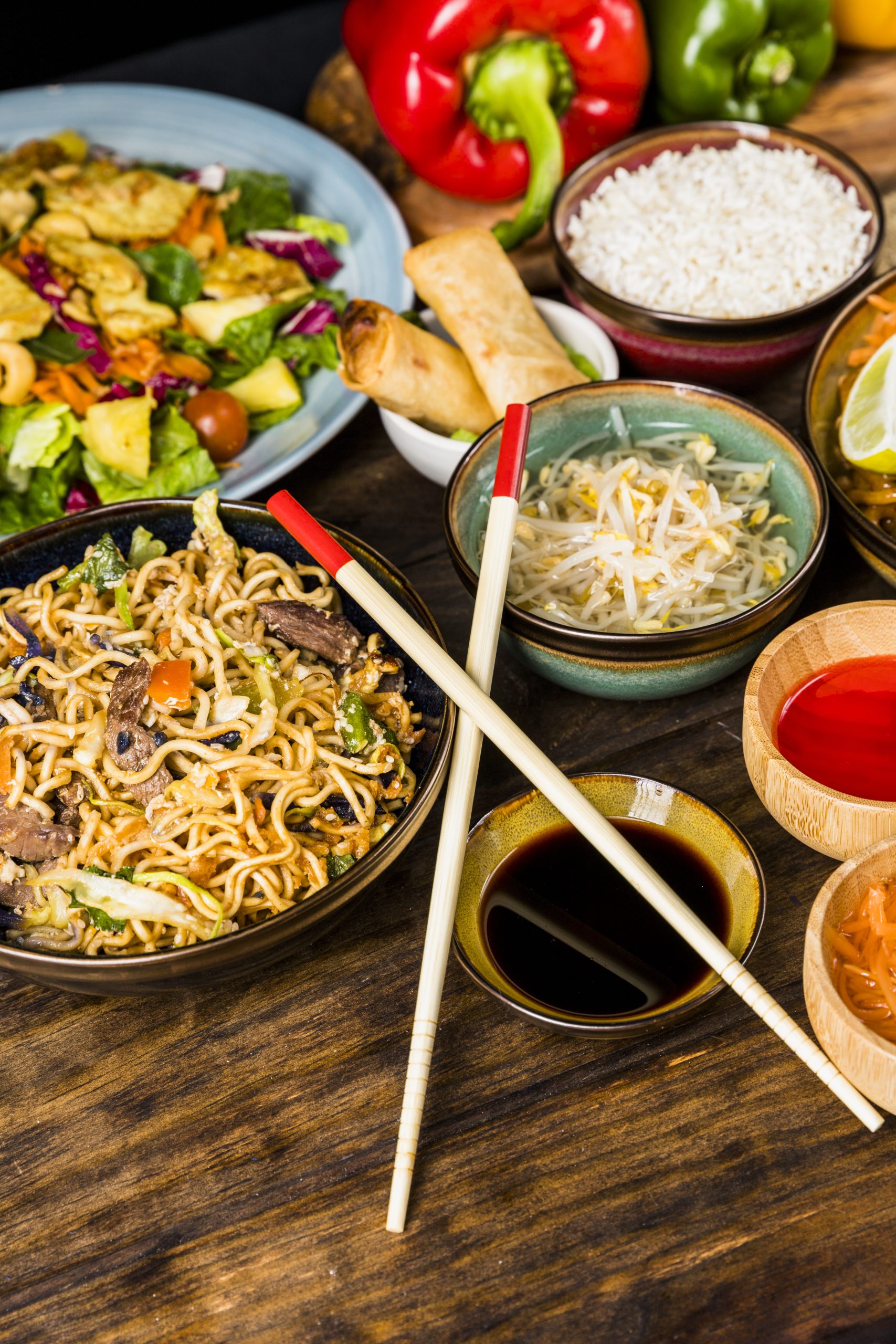 thai-noodles-salad-spring-rolls-rice-beans-sprouts-sauces-with-chopsticks-wooden-table